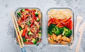 Two tupperware containers full of healthy lunches, next to chopsticks and wooden cutlery