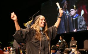Female ACE graduate holding her diploma in the air at commencement