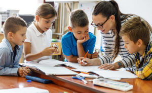 Female teacher works with a small group of four students, demonstrating a lesson