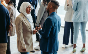 One female professional in a hijab speaks with a Black male professional within a professional setting