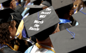 Photo of a row of graduates with a focus on a decorated grad cap that says, "The tassel was worth the hassle"