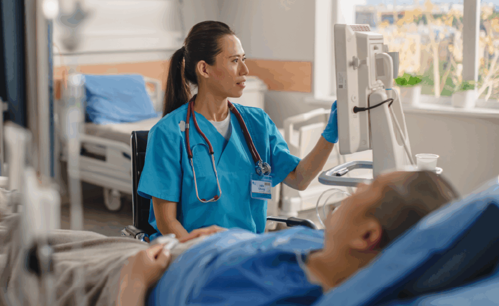 Female nurse sitting beside the bed of a patient, consulting the screen of a monitoring device