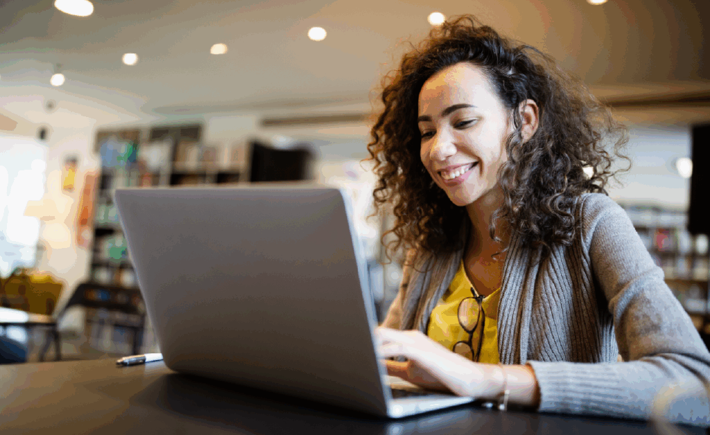Woman with curly hair smiles while working on her laptop at a table