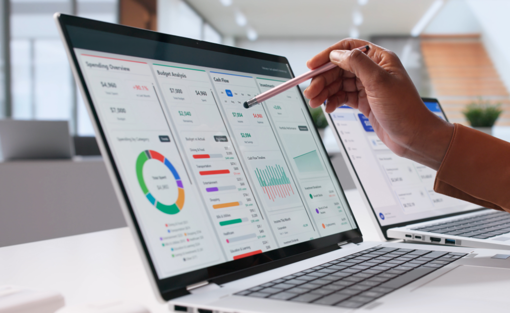 Person pointing at a laptop dashboard with budget charts and graphs