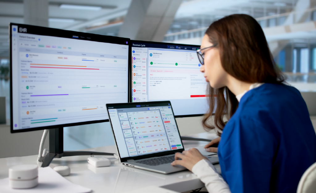 Woman working at a laptop with two large monitors showing business dashboard software