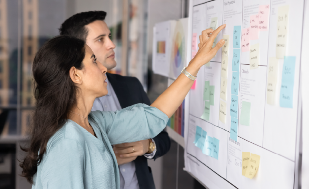 Two coworkers reviewing a project plan on a wall covered with sticky notes