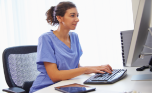 Nurse in scrubs typing at a computer workstation