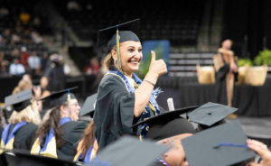 Smiling graduate in cap and gown giving a thumbs up during a college graduation ceremony.