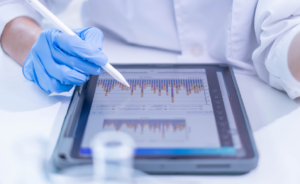 Gloved hand using a stylus to analyze bar chart data on a tablet.