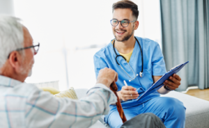 Smiling male nurse in scrubs reviewing a clipboard while talking with an elderly patient.