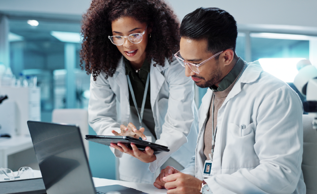 Two public health professionals in lab coats reviewing data together on a tablet.