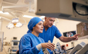 Experienced clinician guides a nursing student using surgical controls in an operating room.